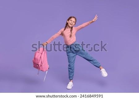 Happy schoolgirl with backpack on violet background