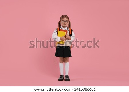 Happy schoolgirl in glasses with backpack and books on pink background