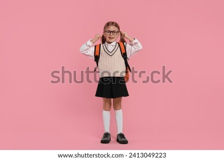 Happy schoolgirl in glasses with backpack on pink background
