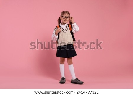Happy schoolgirl in glasses with backpack on pink background