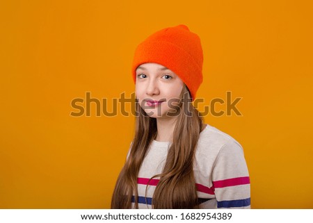 Feliz colegiala con el pelo largo sujeta sus manos delante de un fondo amarillo