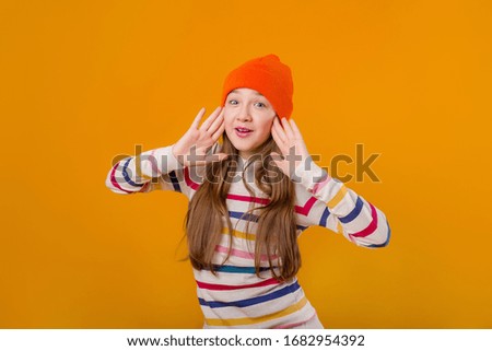 Feliz colegiala con el pelo largo sujeta sus manos delante de un fondo amarillo