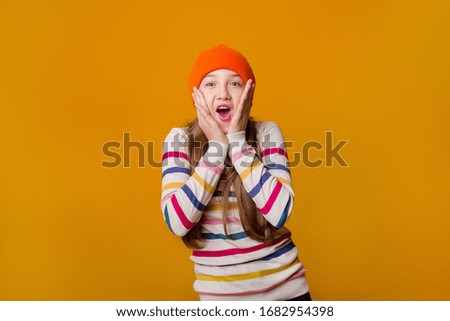 Feliz colegiala con el pelo largo sujeta sus manos delante de un fondo amarillo
