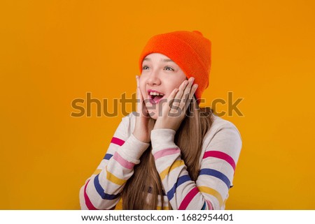 Feliz colegiala con el pelo largo sujeta sus manos delante de un fondo amarillo