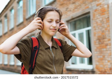 Happy Schoolgirl On The Way To The School. She Is Listening To Music By Headphones. Education And Back To School Concept