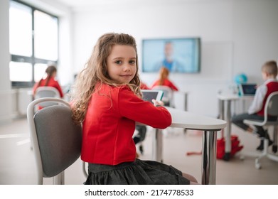 Happy schoolgirl wearing school uniform sitting in class and smiling in the camera.