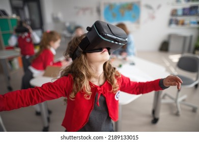 Happy schoolgirl wearing virtual reality goggles at school in computer science class