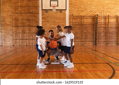 Happy schoolkids and basketball coach forming hand stack at basketball court in school - Powered by Shutterstock