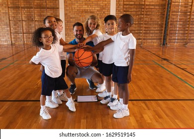 Happy schoolkids and basketball coach forming hand stack and looking at camera in basketball court - Powered by Shutterstock