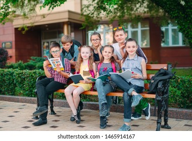 Happy Schoolmates Portrait. Schoolmates seating with books in a wooden bench in a city park and studying on sunny day