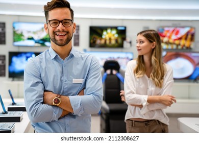 Happy seller man helping to woman to buy a new digital smart device in tech store. - Shutterstock ID 2112308627