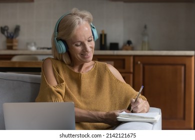 Happy Senior 50s Online Course Student Woman Watching Learning Webinar, Attending Virtual Lesson, Class. Smiling Mature Lady In Big Headphones Using Laptop At Home, Writing Notes, Making Video Call