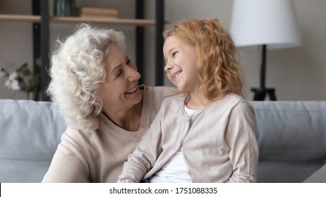 Happy Senior 60s Grandmother And Little Preschooler Granddaughter Relax On Couch In Living Room Talking, Smiling Mature Grandparent And Small Grandchild Have Fun Enjoy Family Weekend Together