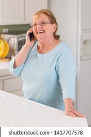 Happy Senior Adult Woman On Her Smart Cell Phone In Kitchen.