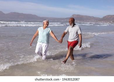 Happy senior african american couple holding hands and having fun on the beach. travel vacation retirement lifestyle concept