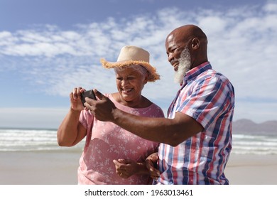 Happy Senior African American Couple Using Smartphone At The Beach. Travel Vacation Retirement Lifestyle Concept