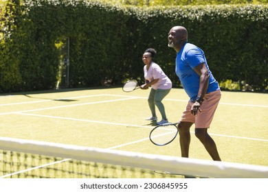 Happy senior african american couple playing tennis doubles on sunny grass tennis court, copy space. Senior lifestyle, retirement, sport, summer, fitness, hobbies and leisure activities. - Powered by Shutterstock