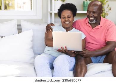 Happy senior african american couple on couch using laptop and embracing in sunny living room. Senior lifestyle, retirement, togetherness, technology, communication and domestic life, unaltered. - Powered by Shutterstock