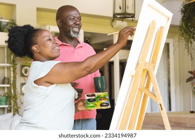 Happy senior african american couple painting canvas on easel together at home. Senior lifestyle, retirement, creativity, hobbies, togetherness, art and domestic life, unaltered. - Powered by Shutterstock