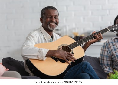 Happy senior african american man playing acoustic guitar on couch in nursing home - Powered by Shutterstock