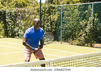 Happy senior african american man playing tennis on sunny grass court. Senior lifestyle, retirement, sport, summer, fitness, hobbies and leisure activities. - Powered by Shutterstock