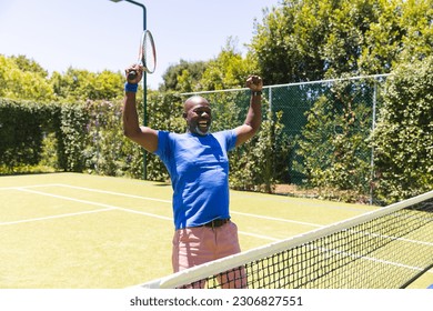 Happy senior african american man playing tennis and celebrating on sunny grass court. Senior lifestyle, retirement, sport, summer, fitness, hobbies and leisure activities. - Powered by Shutterstock