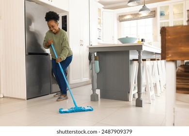 Happy senior african american woman cleaning floor with mop at home. Domestic life, retirement, cleaning and lifestyle, unaltered.