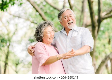 Happy Senior Asian Couple Dancing In The Park In Sunny Day