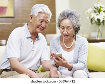 Happy Senior Asian Couple Looking At Mobile Phone At Home, Happy And Smiling