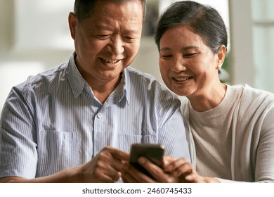 happy senior asian couple sitting on couch at home using cellphone together - Powered by Shutterstock