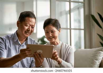 happy senior asian couple sitting on couch at home using digital tablet together - Powered by Shutterstock