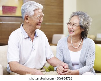 happy senior asian couple sitting on couch talking at home, smiling, holding hands
