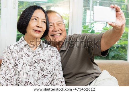 Happy senior Asian couple smiling and taking selfie by mobile smart phone at home