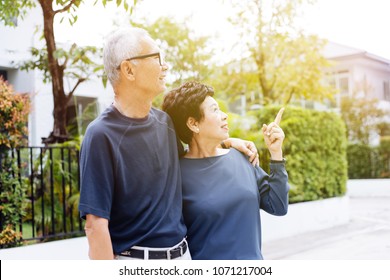 Happy Senior Asian Couple Walking And Pointing In Outdoor Park And House