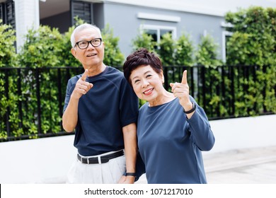 Happy Senior Asian Couple Walking And Pointing In Outdoor Park And House