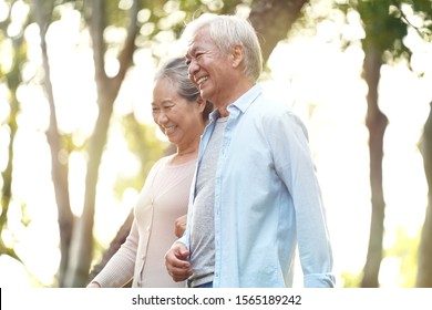 Happy Senior Asian Couple Walking Talking Relaxing Outdoors In Park