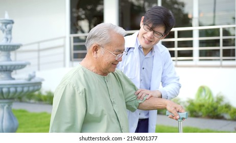 Happy Senior Asian Elder Man Trying To Walk On The Grass Field To Practice In Physical Therapy With A Doctor. Very Old Man Walking On The Grass Field With Barefoot And Using Staff.