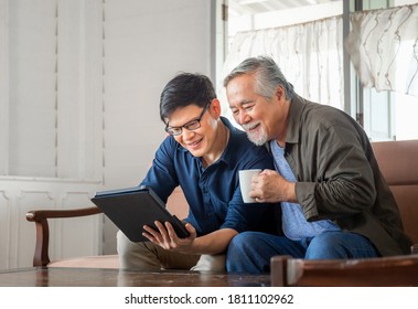 Happy Senior Asian Father And Adult Son Using Tablet Smartphone In Living Room