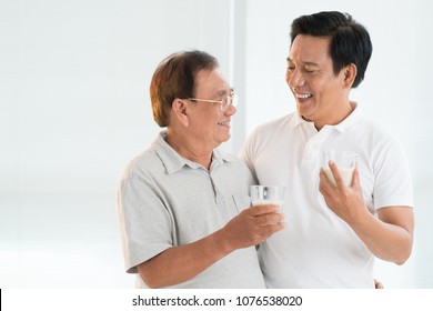 Happy Senior Asian Man Hugging His Adult Son And Drinking Milk