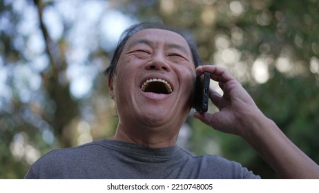 Happy Senior Asian Man Speaking On Phone While Walking In City Street. Portrait Of An Older Middle Aged Person Talking In Conversation With Cellphone Device