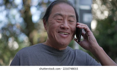 Happy Senior Asian Man Speaking On Phone While Walking In City Street. Portrait Of An Older Middle Aged Person Talking In Conversation With Cellphone Device