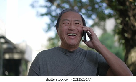 Happy Senior Asian Man Speaking On Phone While Walking In City Street. Portrait Of An Older Middle Aged Person Talking In Conversation With Cellphone Device