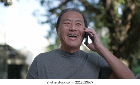 Happy Senior Asian Man Speaking On Phone While Walking In City Street. Portrait Of An Older Middle Aged Person Talking In Conversation With Cellphone Device