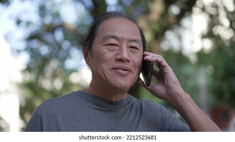 Happy Senior Asian Man Speaking On Phone While Walking In City Street. Portrait Of An Older Middle Aged Person Talking In Conversation With Cellphone Device