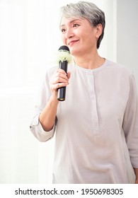 Happy Senior Asian Woman Singing With Microphone.