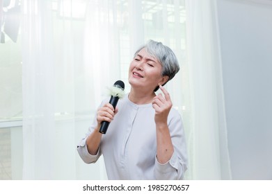 Happy Senior Asian Woman Singing With Microphone.