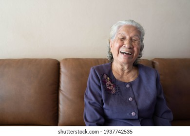 Happy Senior Asian Woman Smiling And Laughing While Sitting On A Couch At Home. Healthy Living For The Elderly Concept.