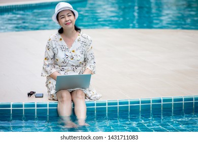 happy Senior asian woman working on  laptop computer sitting at poolside with put her legs in the water . relaxation retirement - Powered by Shutterstock