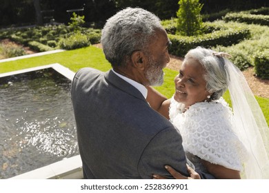 Happy senior biracial bride and groom dancing in garden at sunny wedding ceremony. Marriage, romance, love, tradition, ceremony, summer, retirement and senior lifestyle, unaltered. - Powered by Shutterstock