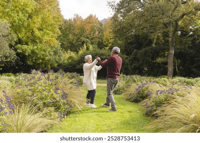 Happy senior biracial couple dancing with flowers around them in garden at home. Senior lifestyle, retirement, nature and domestic life, unaltered. - Powered by Shutterstock